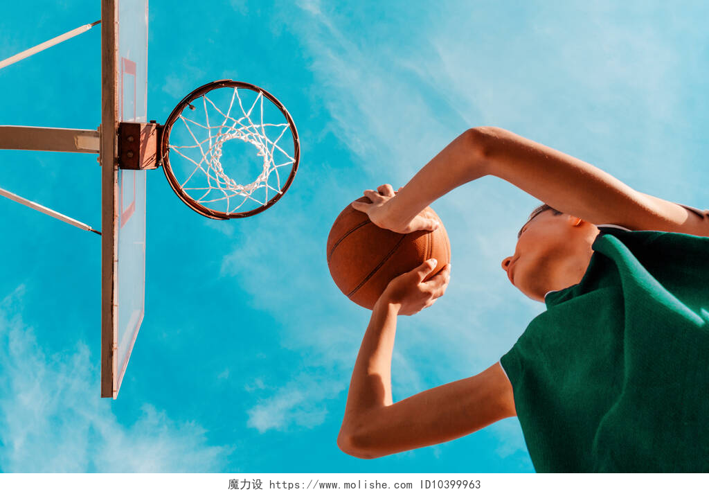 蓝天白云下的篮球架和打篮球的人体育和篮球。一个身穿绿色运动服的少年把球扔进了篮筐。底部的观点。背景是蓝天.